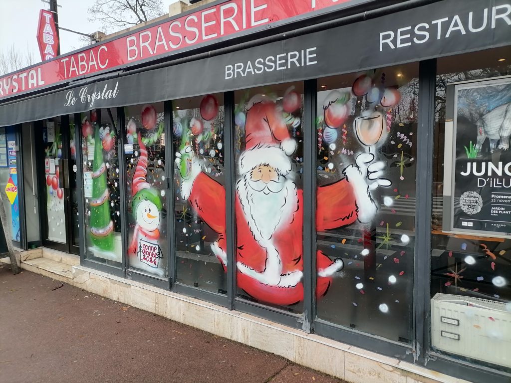 Vitrine de brasserie ornée de décorations peintes à la main avec un thème de Noël, incluant des motifs festifs